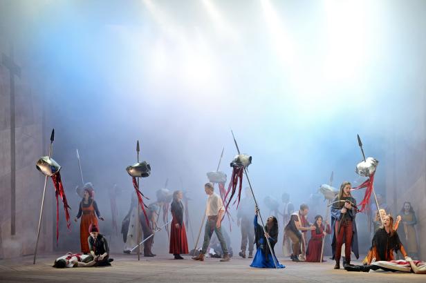 Eine Theaterszene mit Schauspielern in mittelalterlichen Kostümen und Speeren mit Helmen.