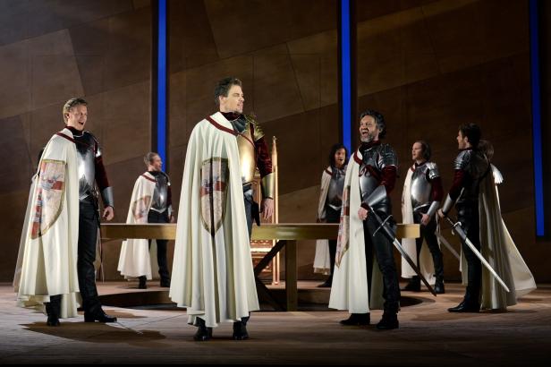 Eine Bühnenszene mit Männern in Rüstungen und Umhängen, die singen.