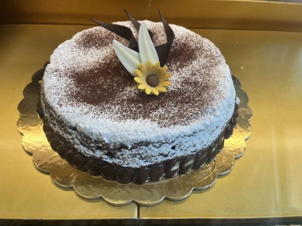 Ein Schokoladenkuchen mit Puderzucker und einer gelben Zuckerblume als Dekoration.