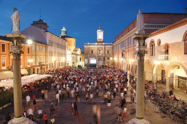 Eine Menschenmenge versammelt sich auf einem belebten Platz in Italien am Abend.