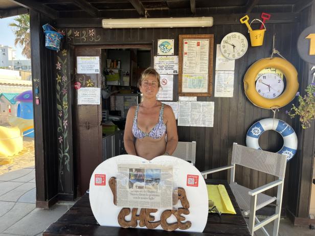 Eine Frau steht in einem Strandkiosk mit Dekorationen wie Uhren und Rettungsringen.