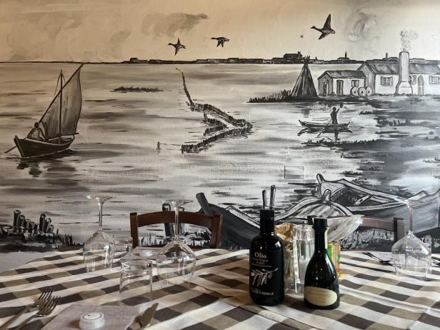 Ein gedeckter Tisch vor einer Wandmalerei mit einer Küstenlandschaft.