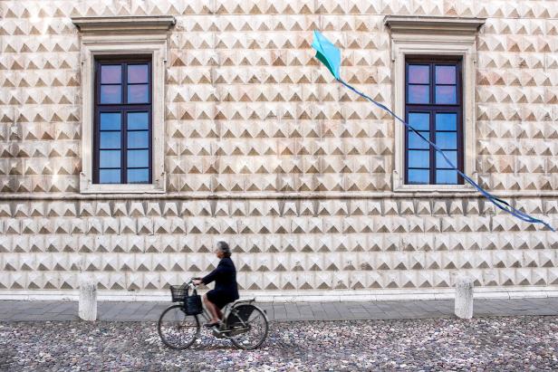 Eine Frau fährt mit dem Fahrrad vor dem Palazzo dei Diamanti in Ferrara, während ein Drachen steigt.