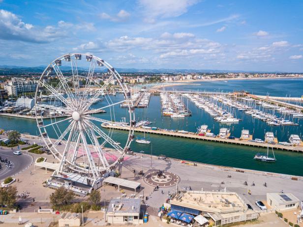 Ein großes Riesenrad steht an einem Hafen mit zahlreichen Segelbooten.