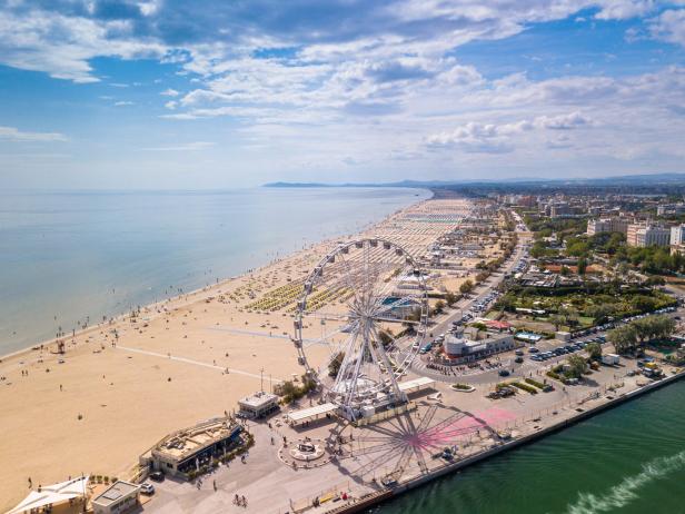 Luftaufnahme eines Strandes mit einem Riesenrad und vielen Sonnenschirmen.