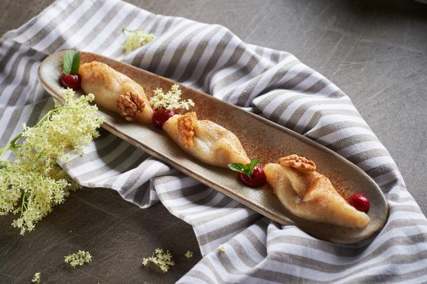 Drei Maultaschen auf einem Teller, garniert mit Kirschen, Walnüssen und Holunderblüten.