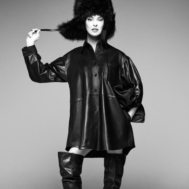 Linda Evangelista posiert in einem Pelzhut, einem übergroßen Hemd und Stiefeln in einer Schwarzweißaufnahme.