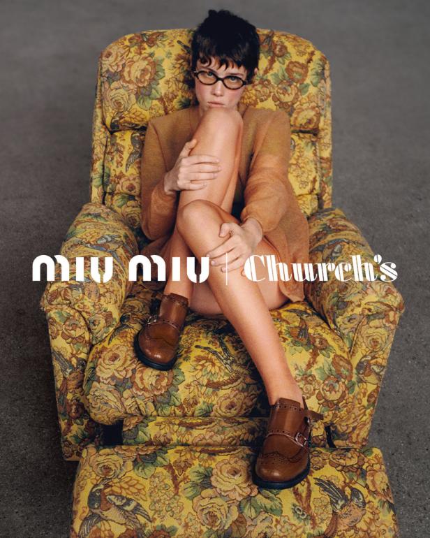 Eine Frau mit Brille sitzt in einem blumigen Sessel und trägt braune Schuhe von Miu Miu und Church's.