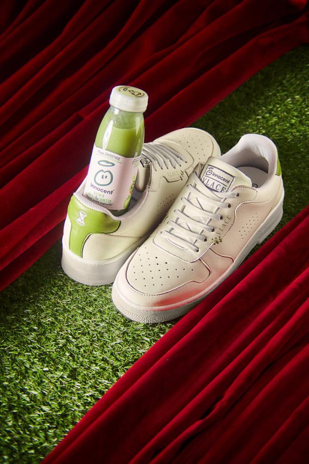 Ein Paar Turnschuhe der Marke „Innocent“ mit einer Flasche Smoothie auf einem grünen Untergrund.