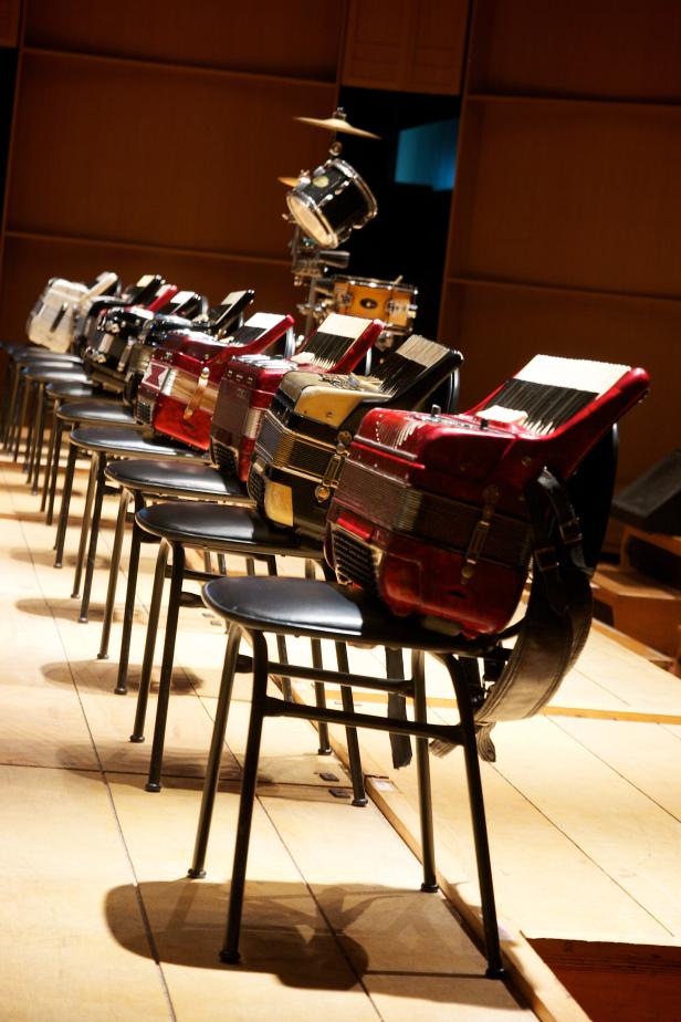 Mehrere Akkordeons stehen auf Stühlen auf einer Bühne bereit.