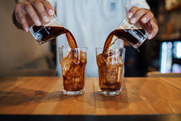 Zwei Gläser werden gleichzeitig mit Kaffee über Eiswürfeln befüllt.