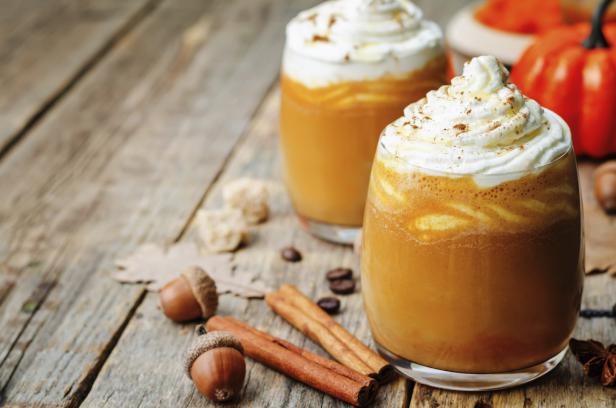 Zwei Gläser Kürbis-Latte mit Schlagsahne und Zimt auf einem Holztisch.