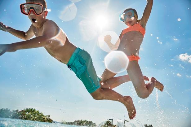 Zwei Kinder mit Taucherbrillen springen ins Schwimmbad.