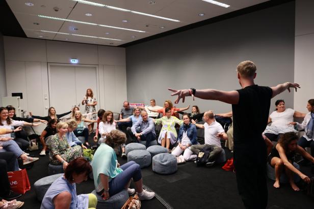 Eine Gruppe von Menschen sitzt in einem Raum und macht Dehnübungen mit einem Trainer.