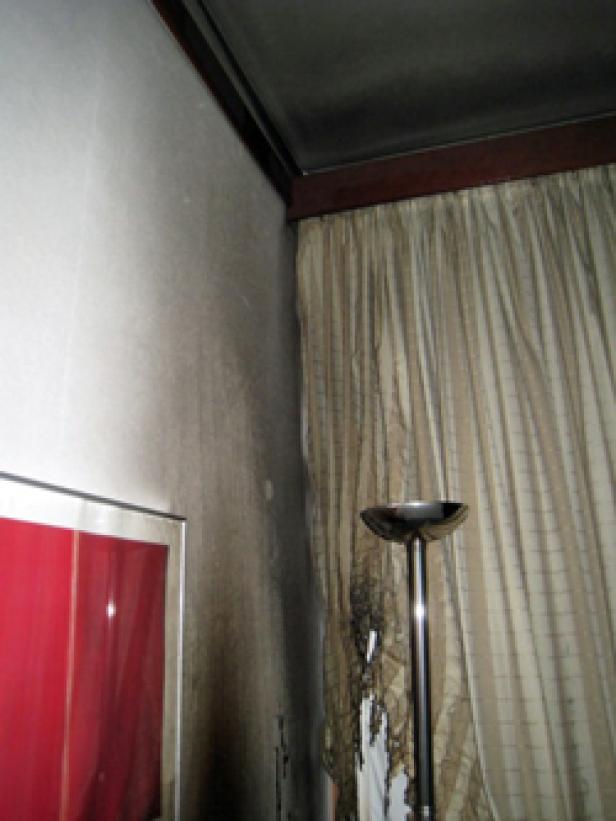 Ein Zimmer mit Brandschäden an Wänden, Decke und Vorhängen.