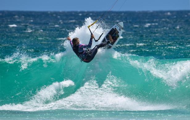 Eine Frau springt mit einem Kiteboard über eine Welle.