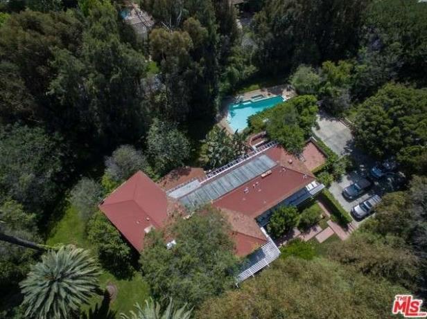 Luftaufnahme eines Hauses mit rotem Dach, Pool und geparkten Autos, umgeben von Bäumen.