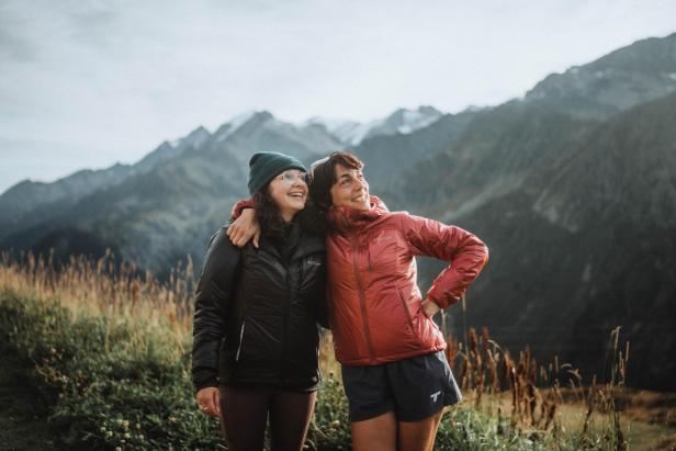 Zwei Frauen umarmen sich vor einer Bergkulisse.