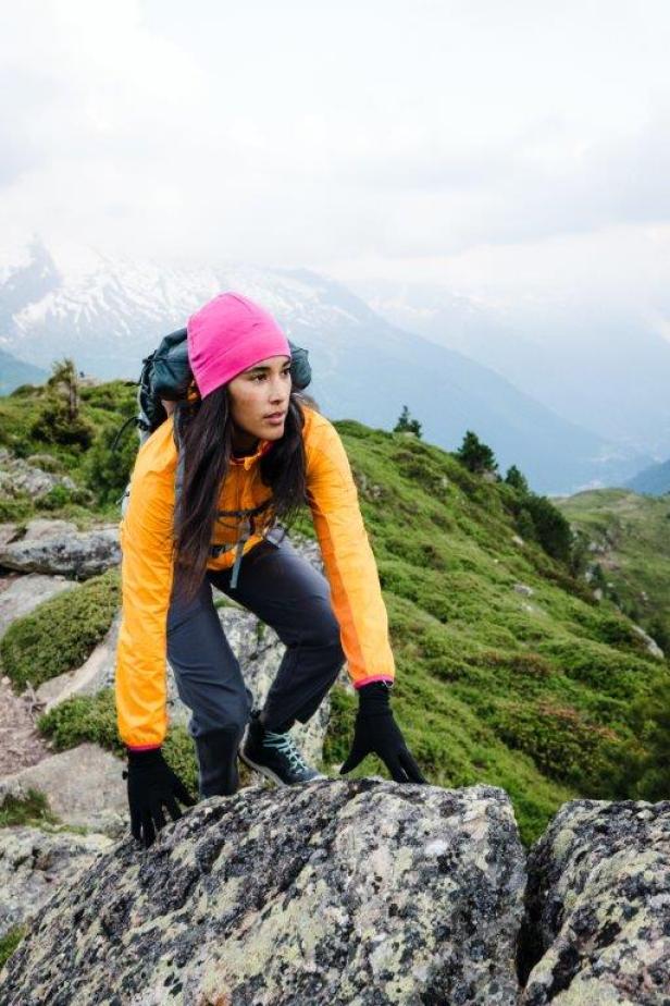 Eine Frau mit Rucksack klettert über Felsen in einer Berglandschaft.