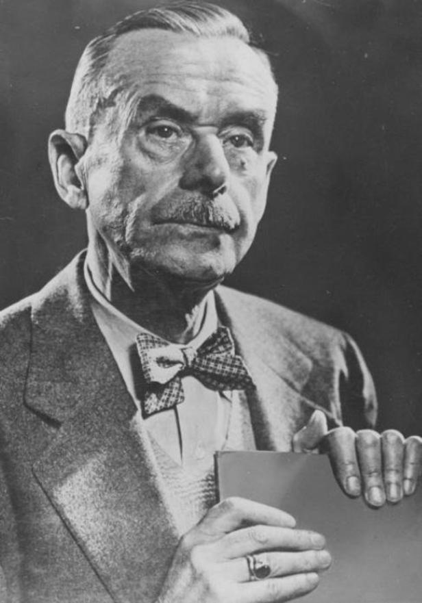 Ein älterer Mann mit Fliege und Anzug hält ein Buch in der Hand.