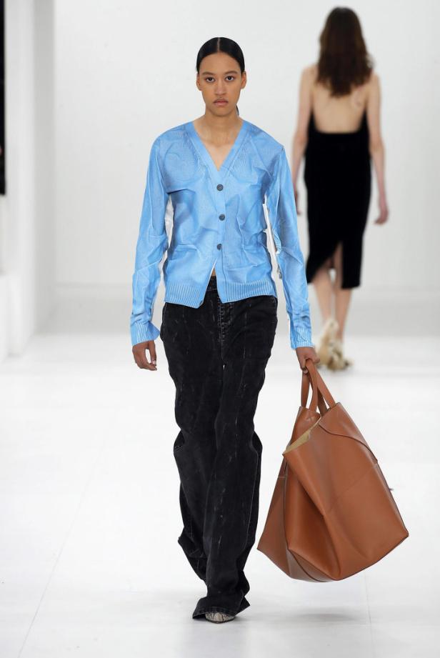 Ein Model präsentiert eine blaue Weste und eine große braune Ledertasche von Loewe.