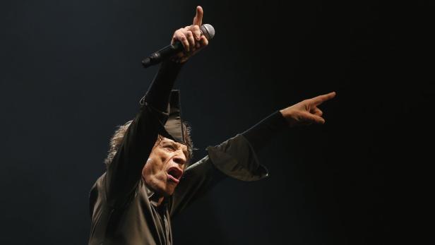 Mick Jagger singt mit erhobenen Armen auf der Bühne.