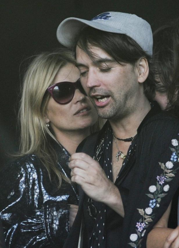 Kate Moss mit einem Mann mit Kappe und offenem Hemd.