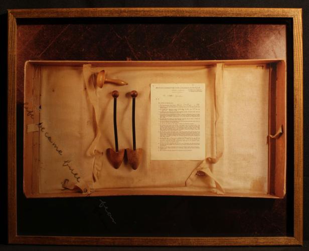 Ein gerahmtes Arrangement mit Schuhspanner, einem Holzkopf und einem Dokument des „British Committee for Children in Prague“.