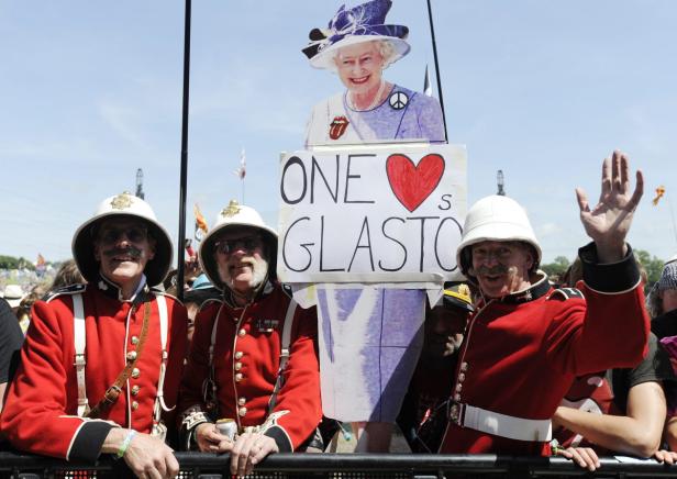 Drei Männer in roten Uniformen halten ein Schild mit einem Bild von Königin Elisabeth II. beim Glastonbury Festival.