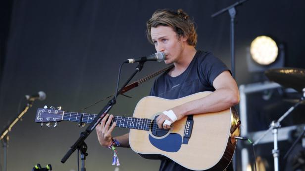 Ein Mann mit Gitarre singt bei einem Konzert ins Mikrofon.