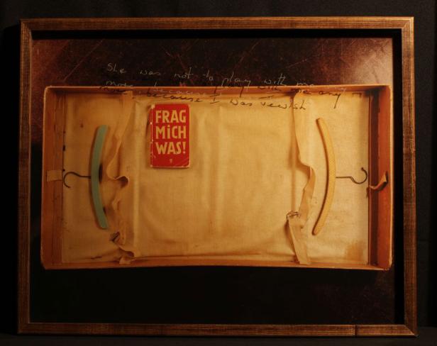 Eine Kunstinstallation mit Kleiderbügeln, einem Buch mit dem Titel „Frag mich was!“ und handgeschriebenen Texten.