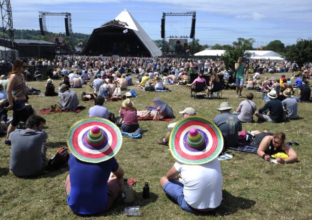 Menschen sitzen und liegen auf einer Wiese vor einer Bühne, einige tragen Sombreros.