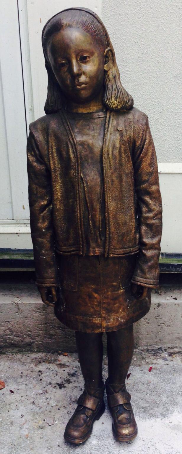 Eine Bronzestatue eines jungen Mädchens in Jacke und Rock.