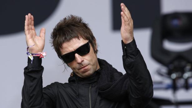 Liam Gallagher mit Sonnenbrille und erhobenen Händen auf der Bühne.