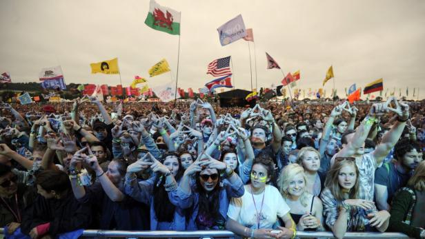 Eine große Menschenmenge jubelt auf einem Festival mit vielen Flaggen im Hintergrund.