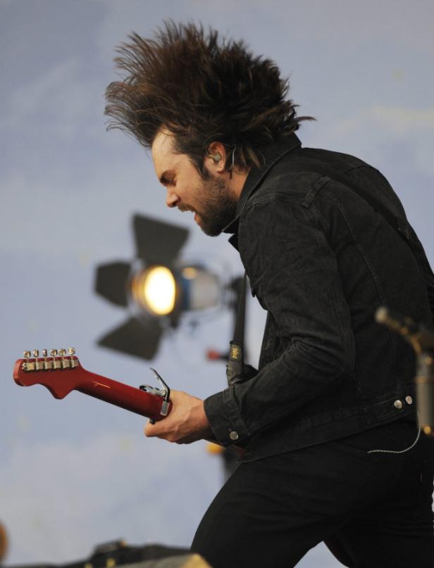 Ein Mann mit hochgestylten Haaren spielt Gitarre auf einer Bühne.