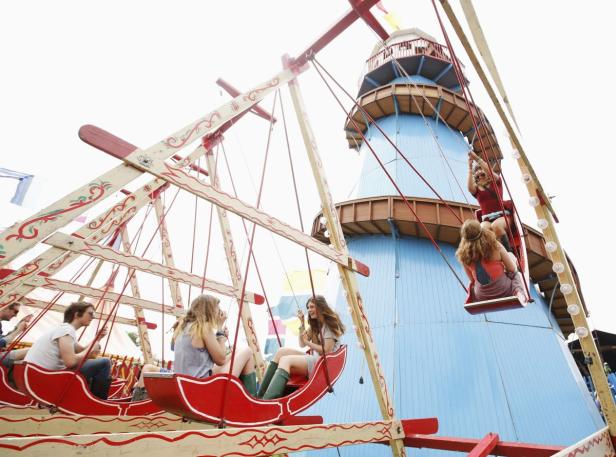 Menschen fahren auf einem Kettenkarussell vor einem blau gestrichenen Turm.