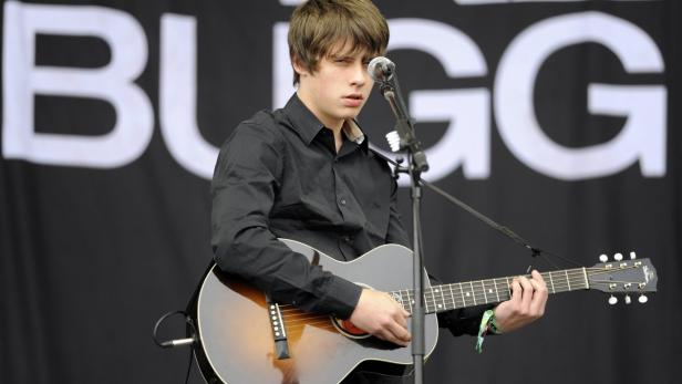 Jake Bugg tritt live mit seiner Akustikgitarre auf einer Bühne auf.