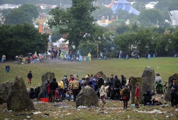 Eine Menschenmenge versammelt sich zwischen großen Steinen auf einem Festivalgelände, das mit Müll übersät ist.