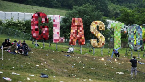Das „Glastonbury“-Schild steht auf einem Hügel voller Müll, während sich Menschen davor aufhalten.
