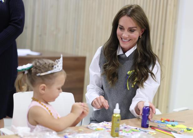 Prinzessin Kate im grauen Pollunder bastelt mit einem kleinen Mädchen, das eine Prinzessinenkrone trägt.