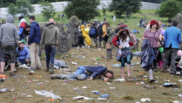 Ein Mann liegt auf dem schlammigen Boden eines überfüllten Festivalgeländes.