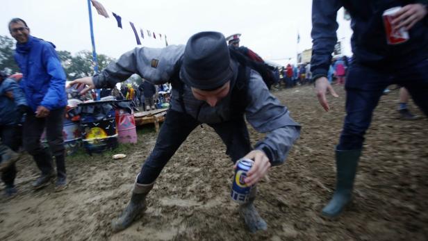 Ein Mann hebt eine Dose Bier im Schlamm auf einem Festival auf.