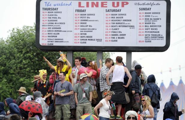 Menschen stehen vor einer Tafel mit dem Line-up des Beat Hotel Glastonbury Festivals.