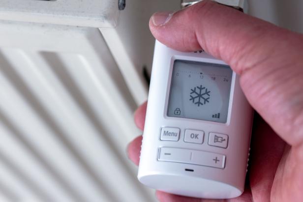 Eine Hand hält einen digitalen Heizkörperthermostat mit Schneeflockensymbol.