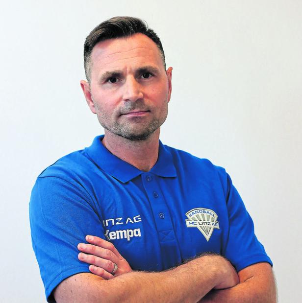 Ein Mann mit verschränkten Armen trägt ein blaues Poloshirt mit dem Logo von HC Linz AG.