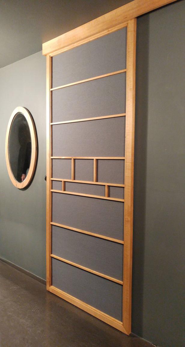 Eine hölzerne Schiebetür mit geometrischem Design vor einer grauen Wand.