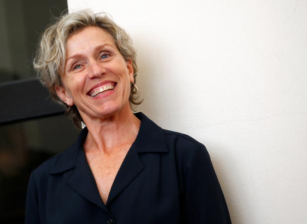Frances McDormand lächelt in einem dunklen Blazer vor einer hellen Wand.