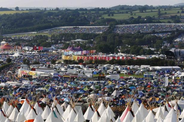 Ein weitläufiges Festivalgelände mit unzähligen Zelten und Bühnen vor einer grünen Hügellandschaft.