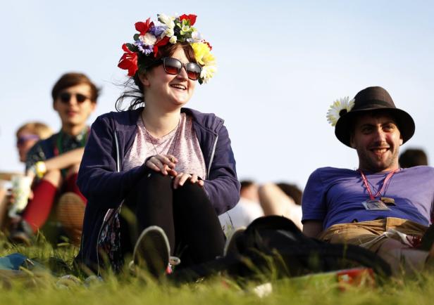 Eine Frau mit Blumenkranz und ein Mann mit Hut sitzen im Gras.
